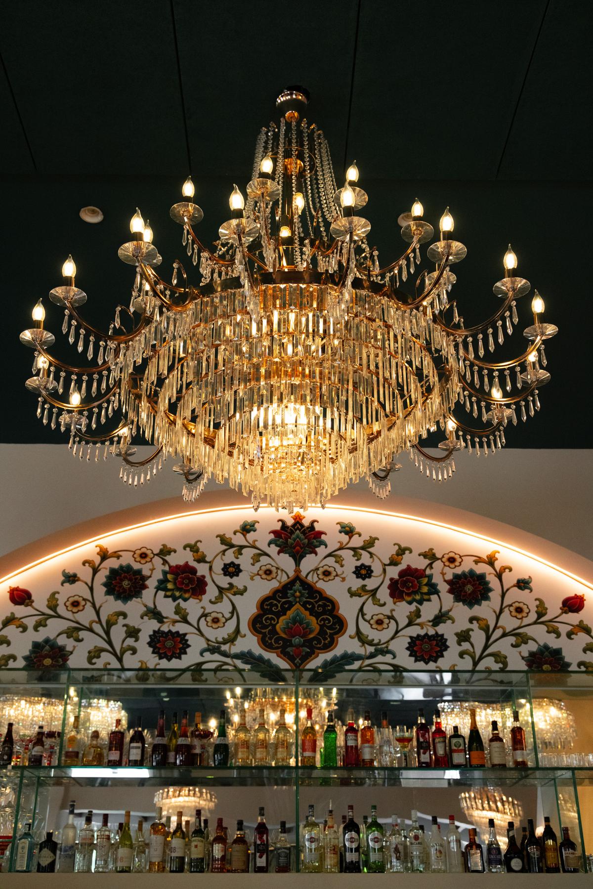 The grand chandelier over the arched bar mural, lit for evening