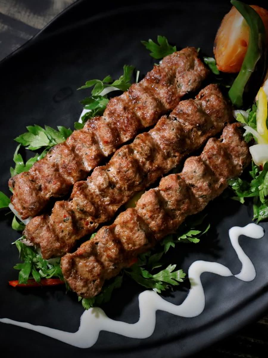Charcoal-grilled koobideh skewers plated with herbs and grilled vegetables